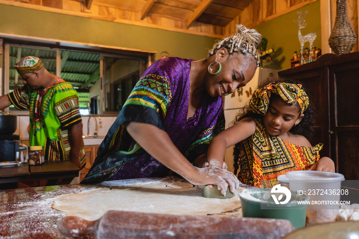 Imagen horizontal de una madre afrocaribeña en el interior de su hogar, cocinando junto a su pequeña