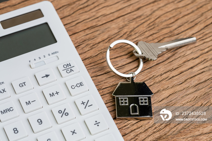 Home key with house keyring or keychain with white calculator on wooden table using as mortgage calc