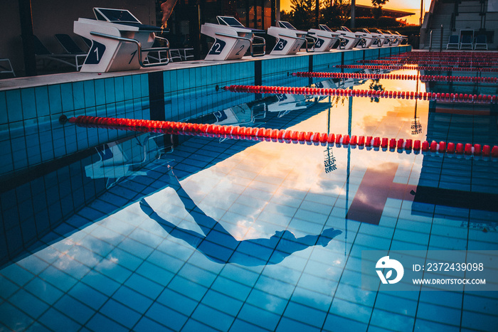 Swimmer jumping to the swimming pool. Reflection in blue water