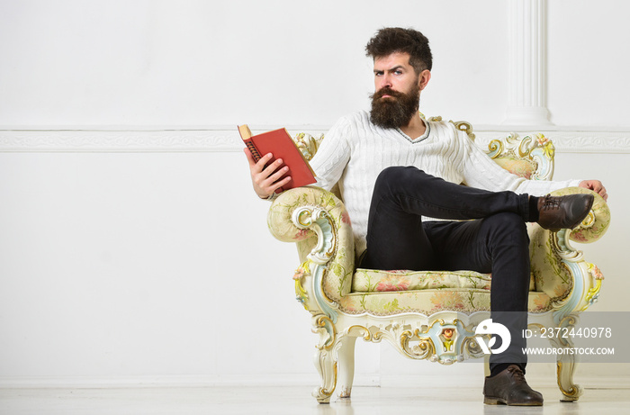 留着胡子和小胡子的男人坐在扶手椅上看书，白墙背景。马乔在leisur度过