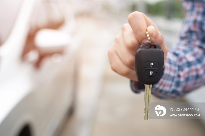 Car key, businessman handing over gives the car key to the other man on car background.