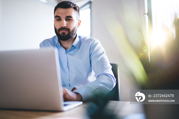 Confident millennial bearded businessman typing on laptop computer sitting at working place sending 