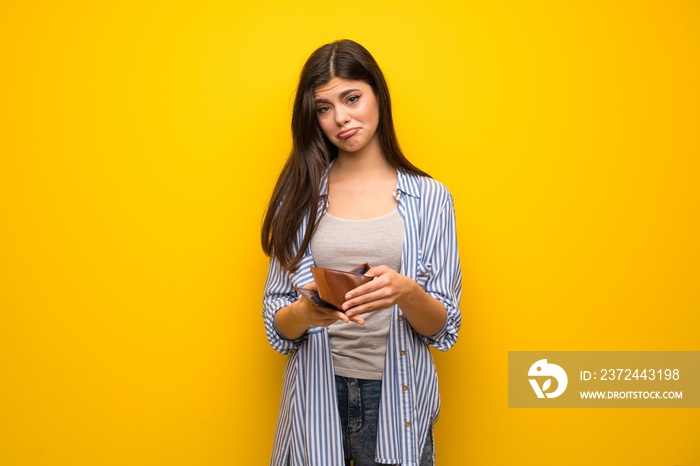 Teenager girl over yellow wall holding a wallet