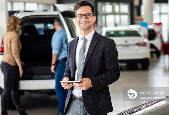 Portrait of young car salesman at dealership salon, looking at camera.