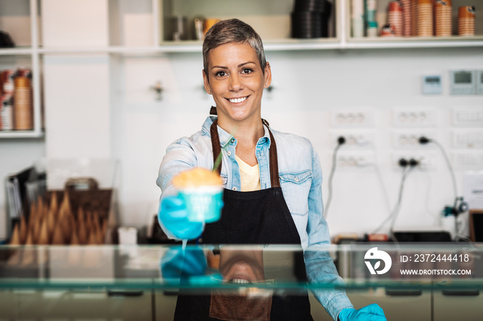 Young and happy saleswoman in black apron selling handmade ice cream at the counter of the pastry sh