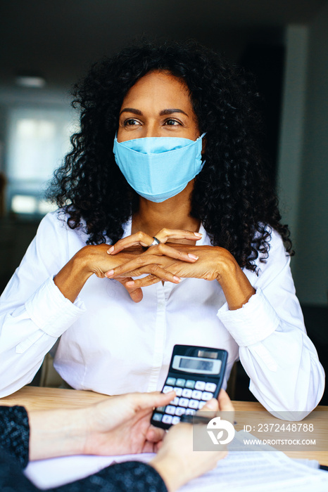 Portrait of a happy business woman sitting at desk with mask and financial advisor holding calculato