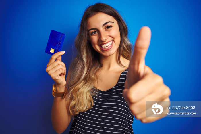 蓝色背景下拿着信用卡的年轻美女开心地笑着做o