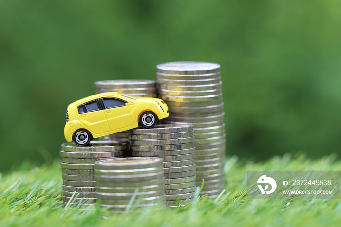 Miniature yellow car model on growing stack of coins money on nature green background, Saving money 