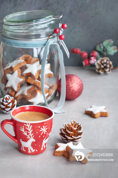 Coffee in red Xmas cup and tasty star ginger cookies in a glass jar with winter decorations