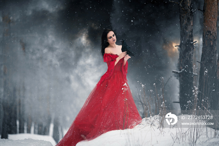 Woman witch in red dress and with raven in her hands in snowy fo