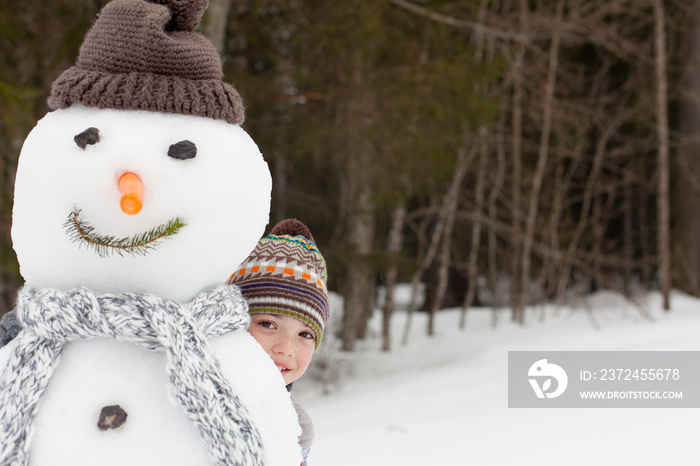 Portrait cute boy hiding behind snowman in snowy woods