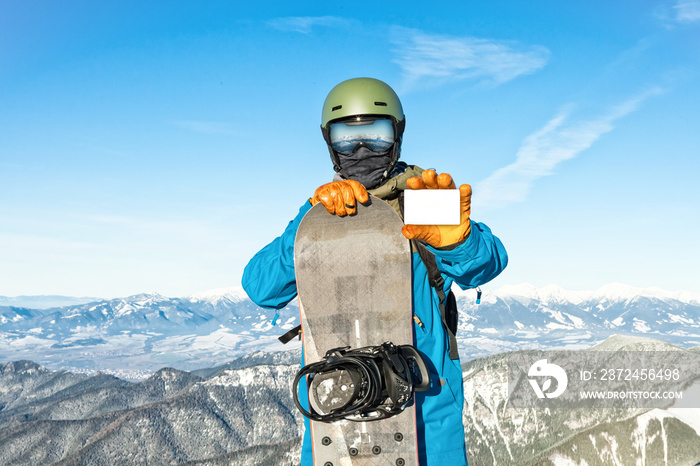 年轻的单板滑雪运动员拿着背景是美丽的山脉的空白滑雪通行证