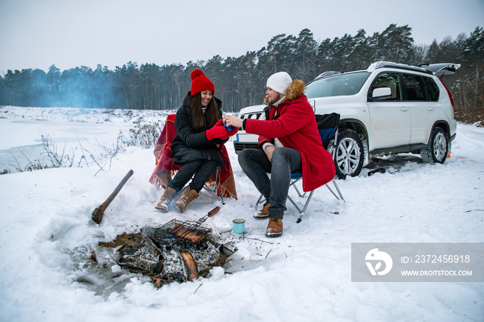 man with woman sitting on chairs near camp fire in winter time. car travel.