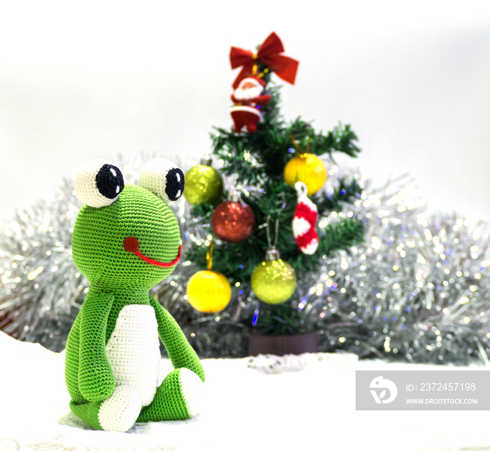 little green frog sitting on white snow in front of Christmas tree waiting happy party, happy concep