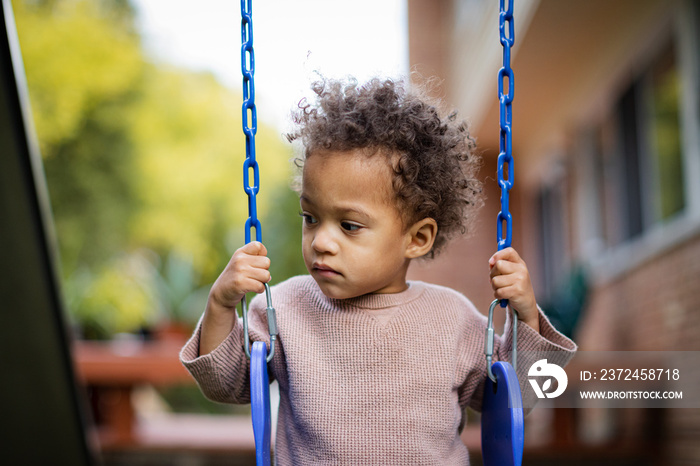 Biracial toddler plays on blue swings in backyard in fall