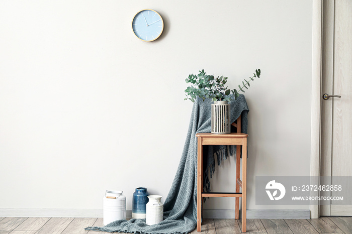 Vase with green eucalyptus branches and plaid on chair near white wall