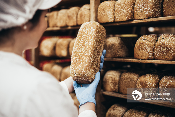 Young female worker working in bakery. She puts bread on shelf.