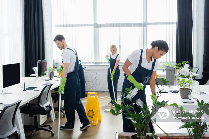 Multiethnic cleaners working with cleaning supplies in office