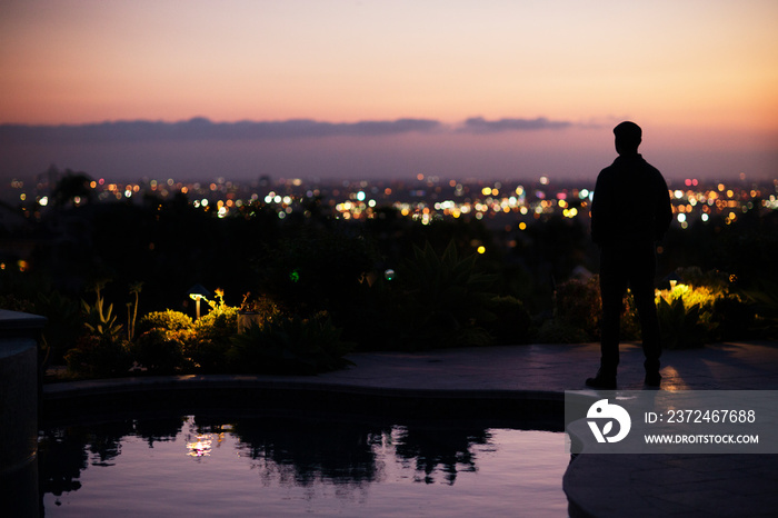 Silhouette of man standing by swimming pool on patio at dusk