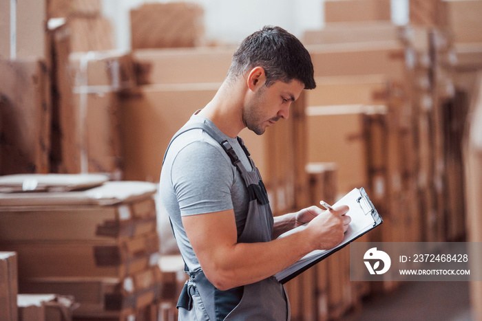 Storage worker in uniform and notepad in hands checks production