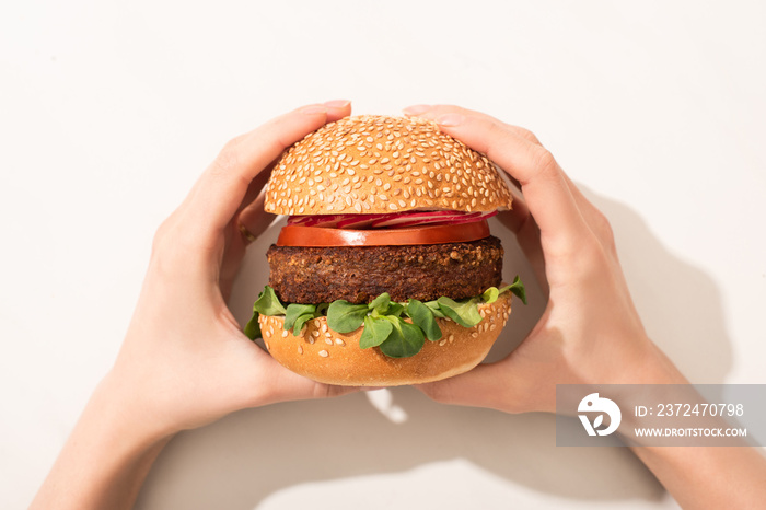 cropped view of woman holding delicious vegan burger with radish on white background