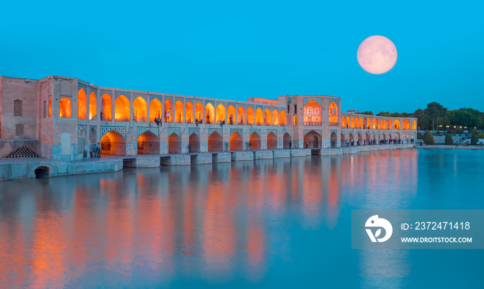 People resting in the ancient Khaju Bridge at twilight blue hour with full moon - Isfahan, Iran  Ele