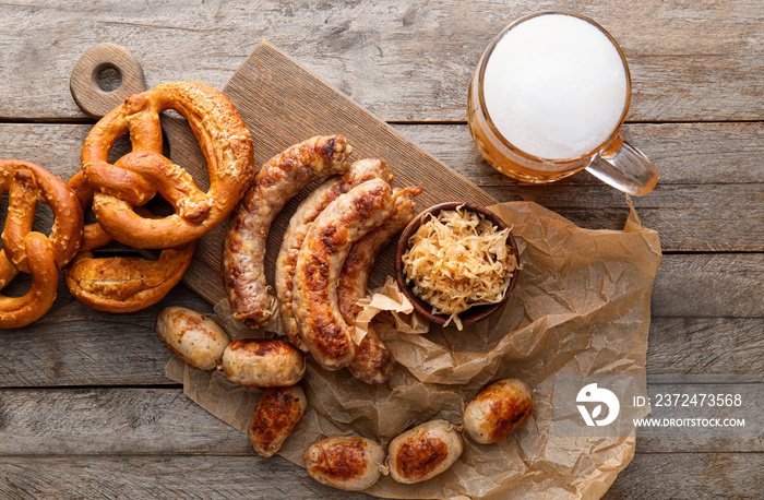 Mug of cold beer, board with Bavarian sausages and snacks on wooden background. Oktoberfest celebrat