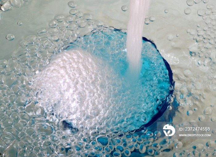 Overflowing water in a blue glass, full overflow glass with water and bubbles