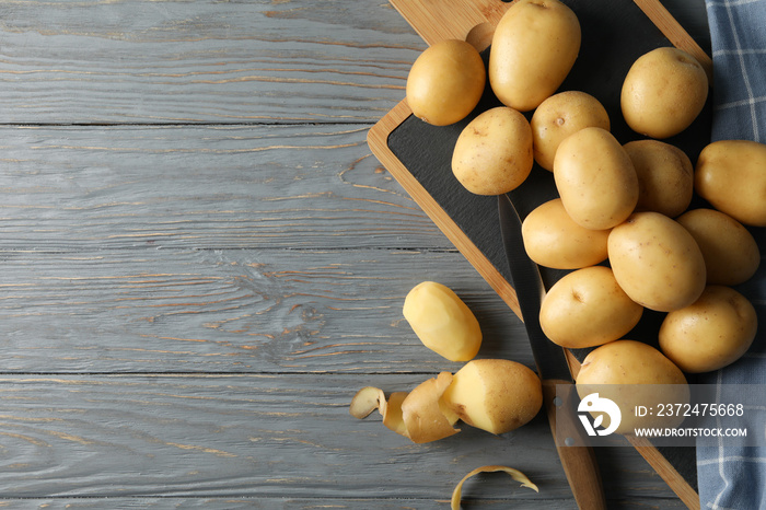 Young potato, board, towel and knife on wooden background, top view