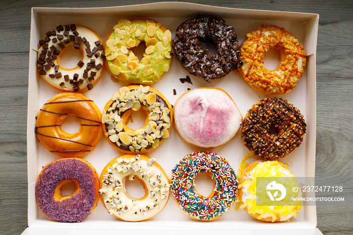 Top view flat lay of a colorful group of twelve delicious donuts in a white paper box on a wooden ta