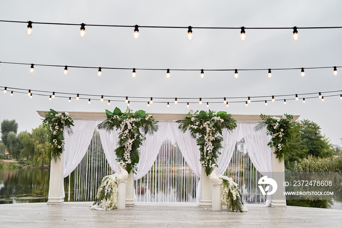 Luxury wedding arch decorated with palm leaves, orchid flowers, floral peacocks and bulbs garland ou