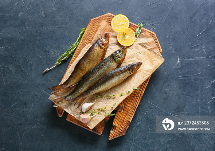 Wooden board with smoked herring fishes on black background