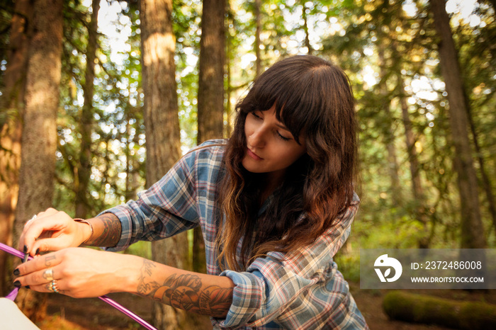 Young woman setting up tent in forest