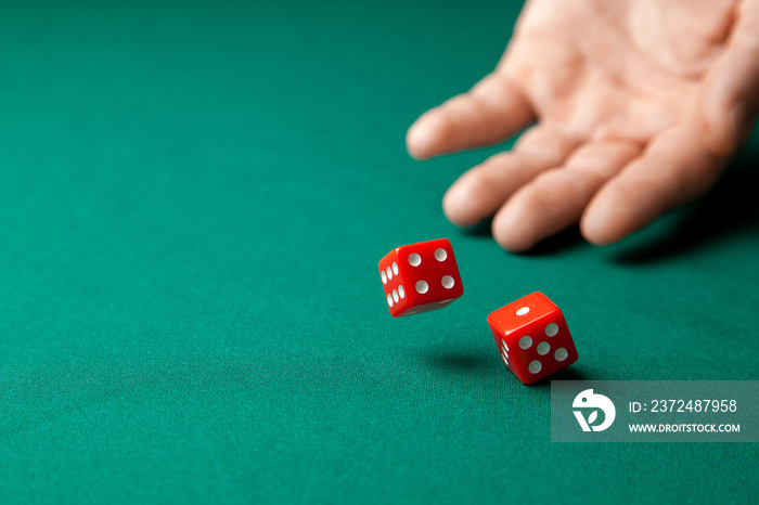 Man holds two red dices and throws them on green poker gaming table in casino. Concept of online gam