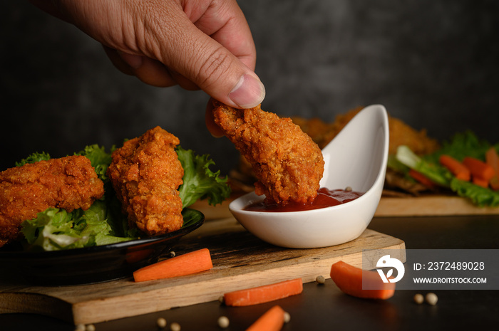 Hand holding crispy fried chicken dipped in tomato sauce.