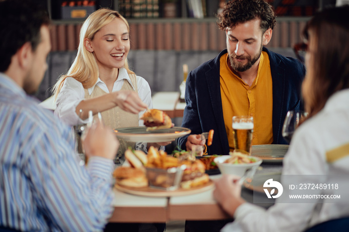 Multiethnic friends sitting at restaurant, drinking alcohol, chatting and having burgers for dinner.