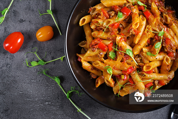 Penne pasta in tomato sauce with meat, tomatoes decorated with pea sprouts on a dark table. Top view