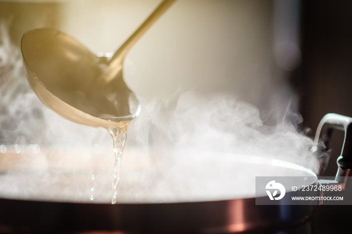 Cooking person in the restaurant is cooking while using the dipper in a large soup pot. And the wate