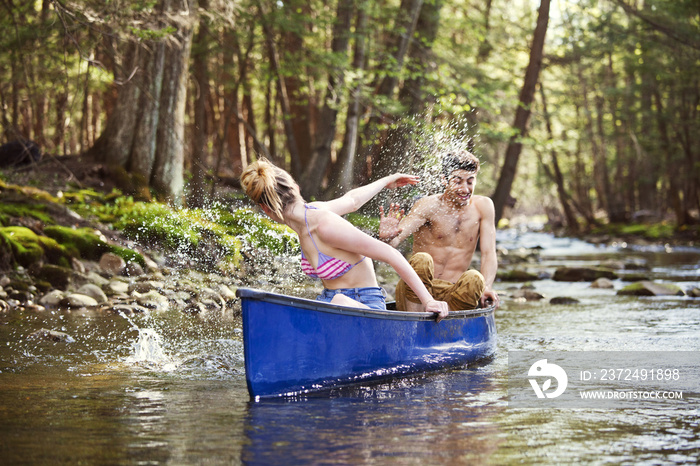 Woman splashing water on boyfriend in canoe