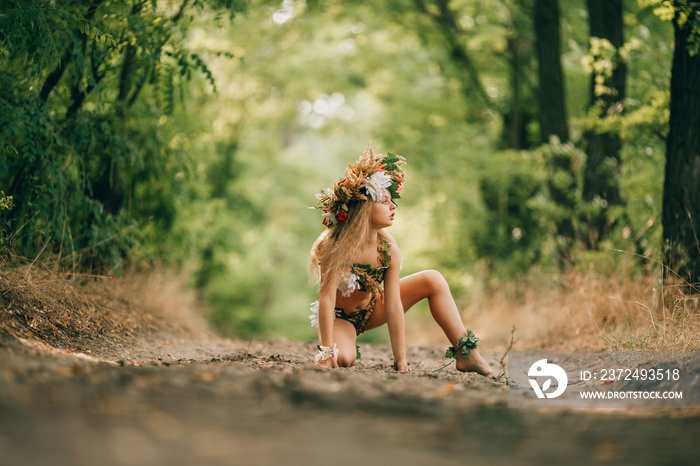 Beautiful little girl in image of nymph dryad sits in forest road.