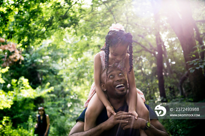 Smiling father carrying his daughter on shoulders in forest