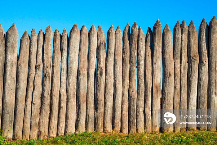 Fence made of sharp wooden stakes against the blue sky. Wooden fence vertical logs pointed against t