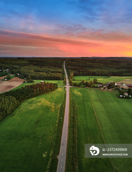 Aerial view of a rural road. The road passes by agricultural fields and through the forest.