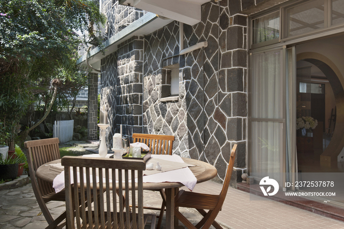 Veranda table and wooden chairs in front of stone walled house