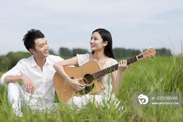 草地上的年轻情侣弹奏吉他