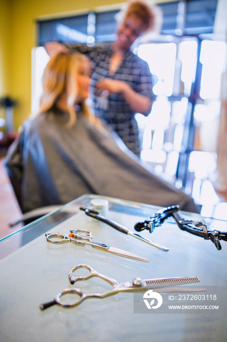 发型师在美发沙龙为女性理发，重点放在前景中的剪刀上