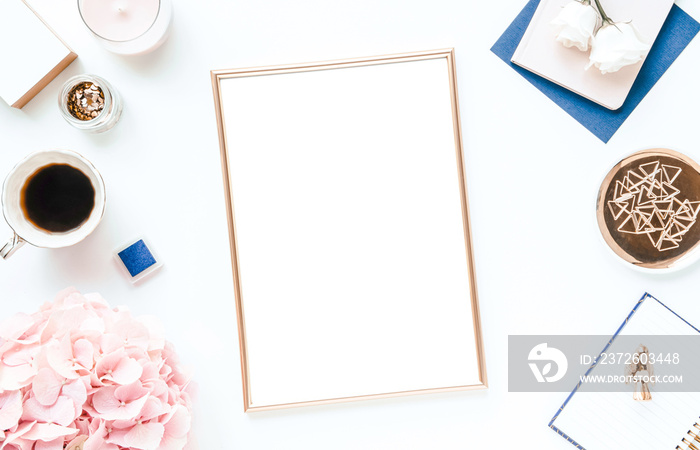 Styled flat lay with various desk items in gold and navy blue colors, pink hydrangea, A4 frame mock-