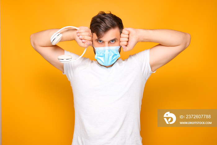 a man in a medical mask holds a white and musical headphones in his hands and gestures emotionally.