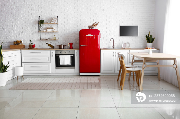 Interior of light kitchen with red fridge, white counters and dining table