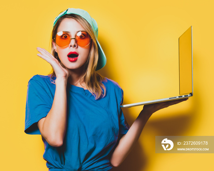 Young style girl with orange glasses and laptop computer on yellow background. Clothes in 1980s styl